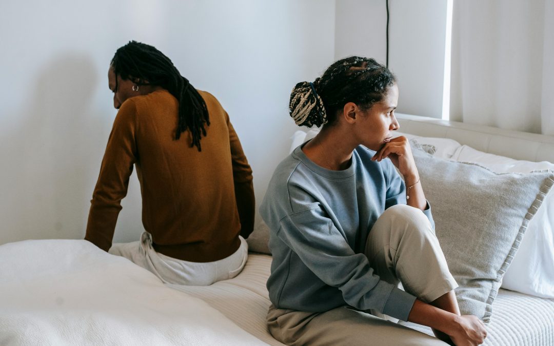 Man and woman look distressed whilst sat back to back on a bed