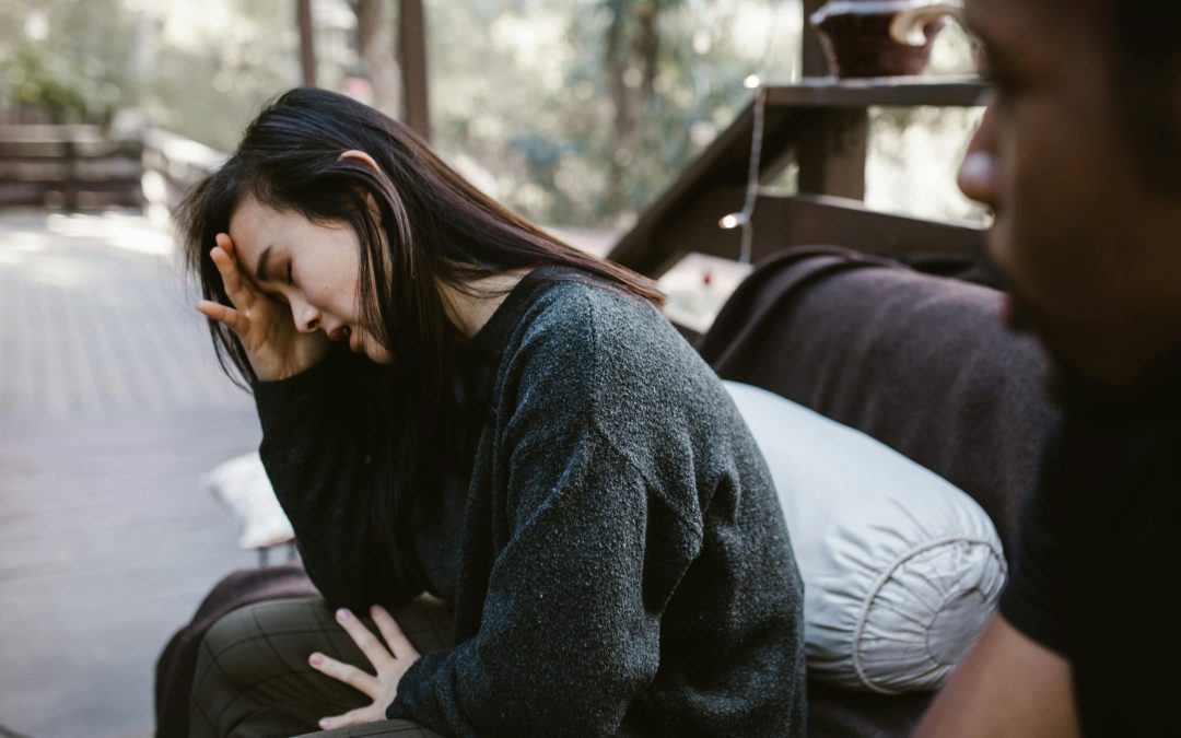 Woman sits on a couch with her head in her hand and could be experiencing reactive abuse.